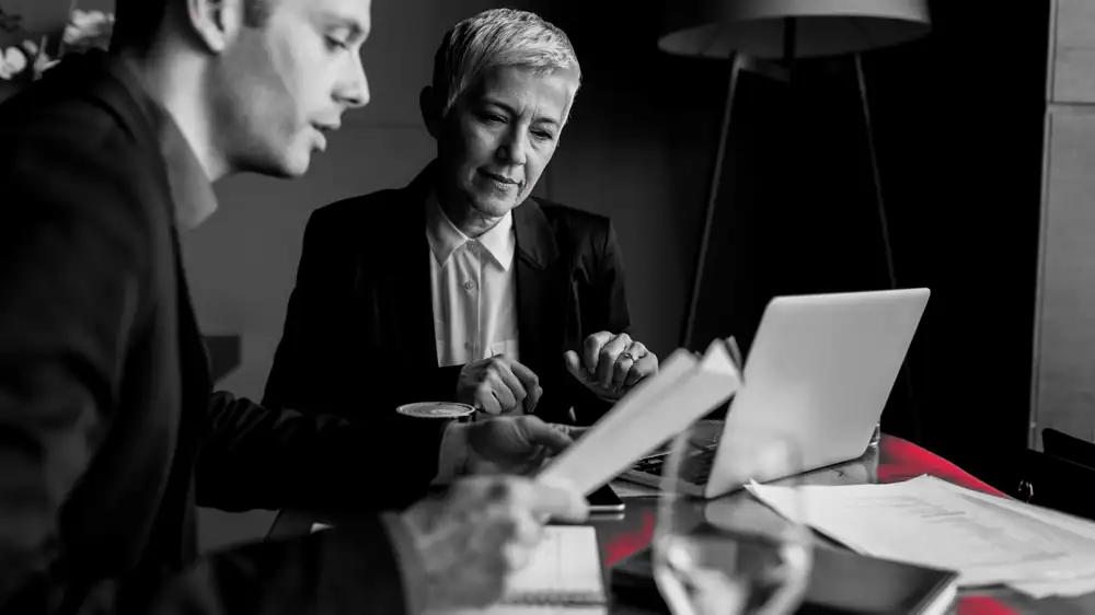 Two professionals reviewing client documents at a desk, the confidential work firms are trusted to protect