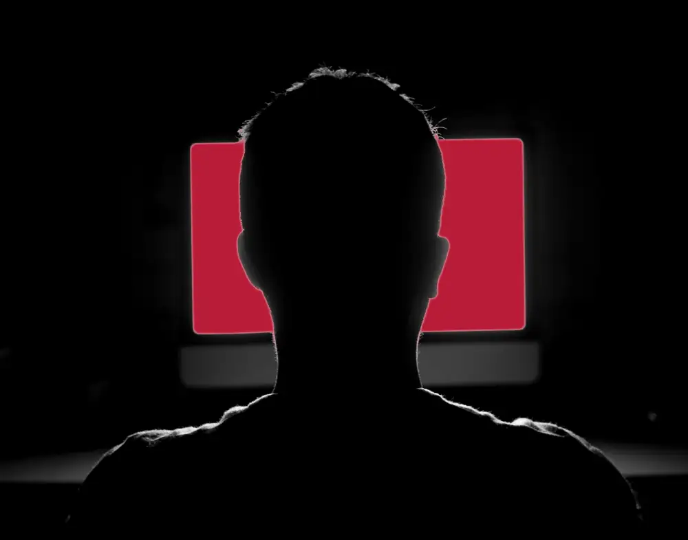 The silhouette of a person facing a glowing screen in a dark room, the outside attacker a black box penetration test simulates