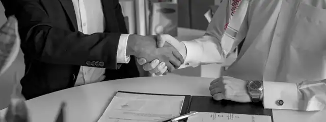 A handshake over signed deal documents